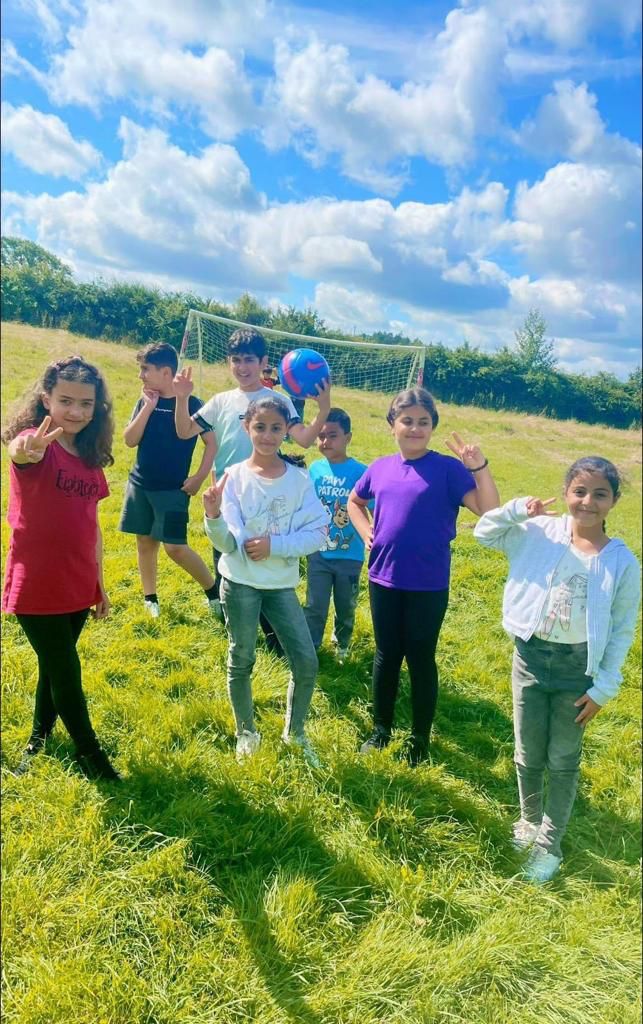 Children posing for a photo on a grassy pitch on a sunny day